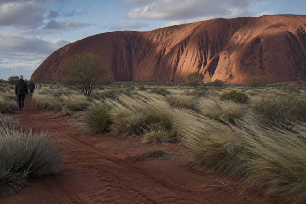 The western face of Uluru seen from the ground across red earth and low scrub