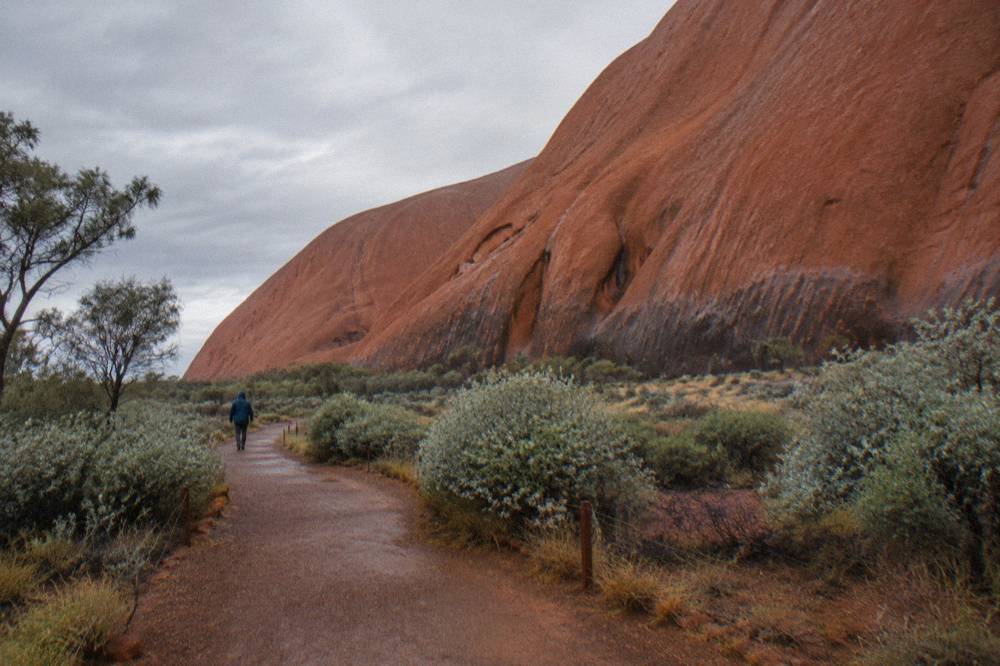 Signposted walking track along the base of Uluru with smooth rock walls rising above