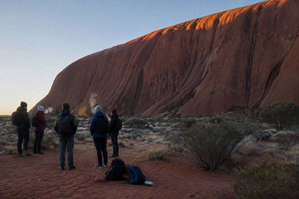 Travellers on a guided small-group tour walking beside tall rock walls at the base of Uluru