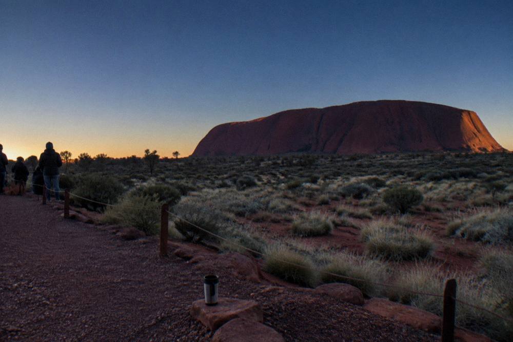 First light glowing on the flanks of Uluru seen from a dune viewing platform
