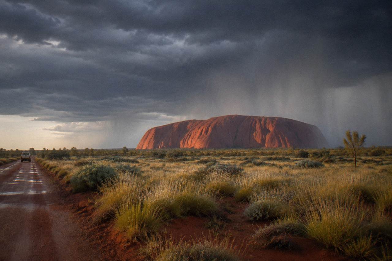 Uluru rising above red sand and spinifex plains under a wide open sky