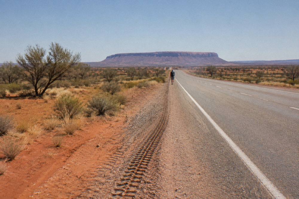 Open highway crossing flat red desert plains with sparse scrub and a distant mesa