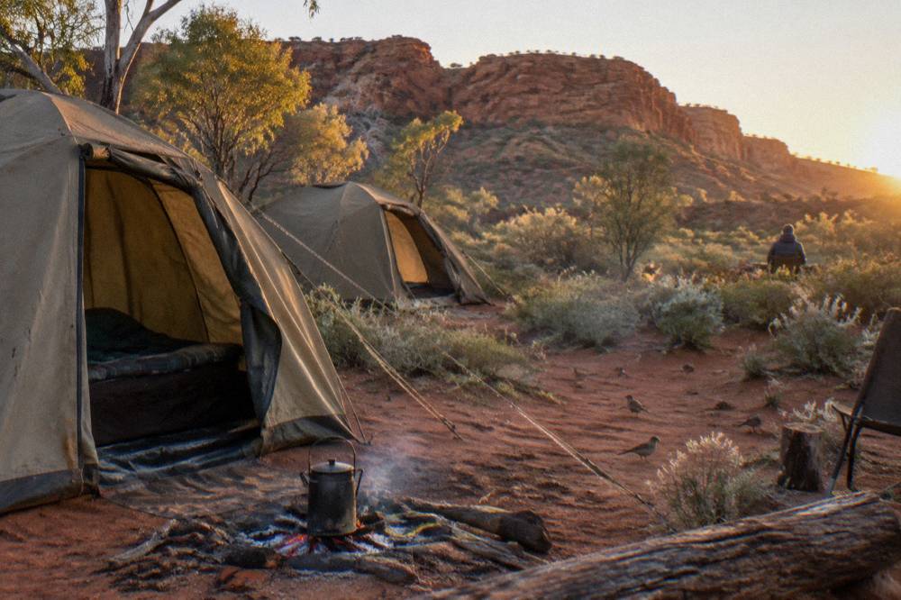 Canvas dome tents and swags set out on red earth beside a desert campfire
