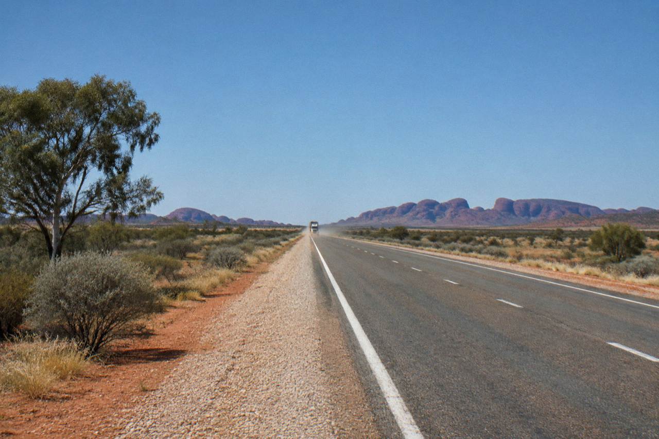 Red desert highway stretching toward distant rock formations under a wide blue sky