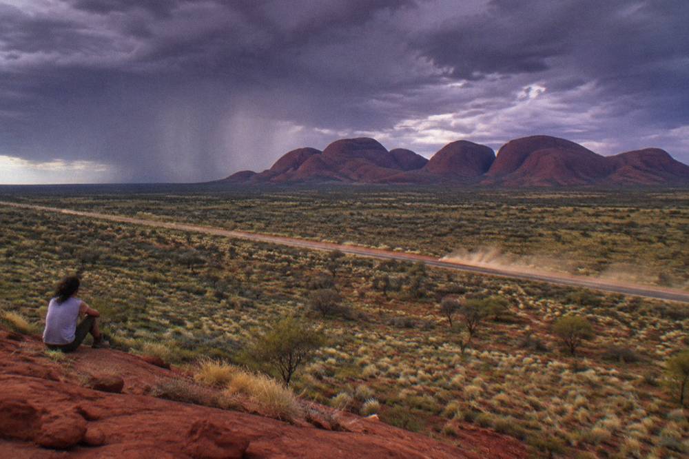 An empty sealed road stretching across red desert plain toward distant rock formations