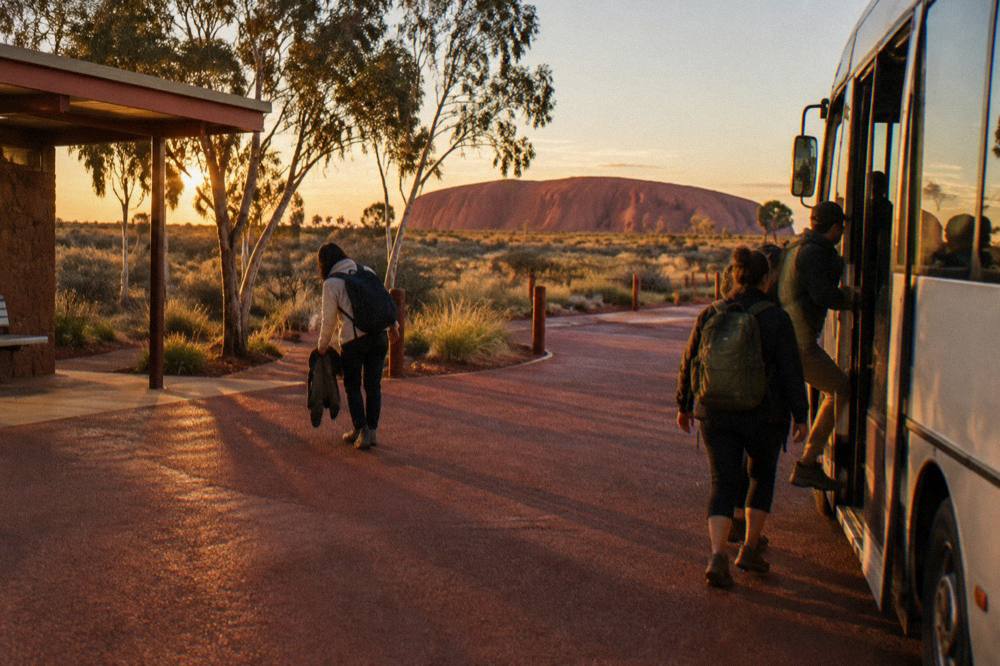 Travellers boarding a small shuttle bus at a resort forecourt in warm evening light