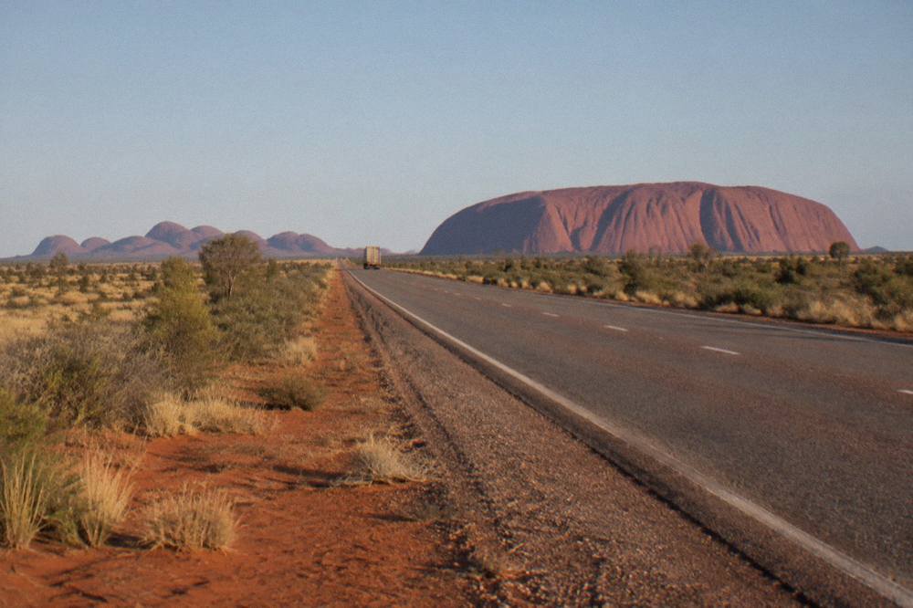 Desert road approaching the Uluru-Kata Tjuta National Park entry station with red sand and spinifex
