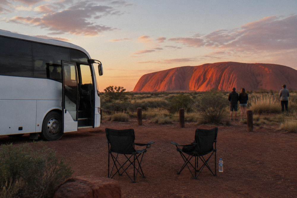 Tour coach parked at a roadside viewing bay with Uluru rising in the background