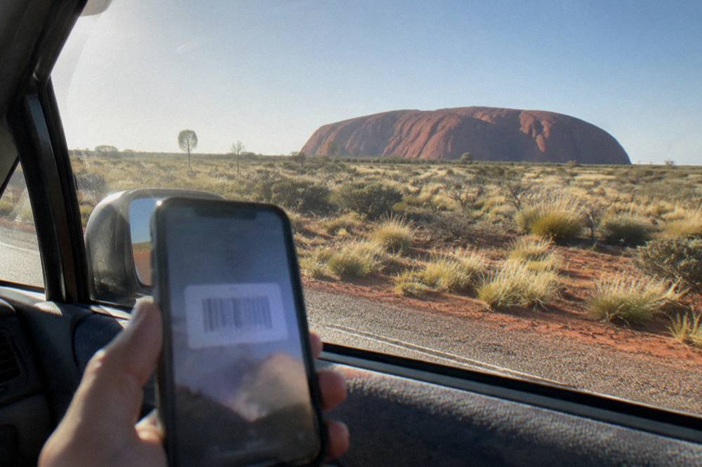 Smartphone displaying a park entry pass barcode held up at a vehicle window beside desert scrubland