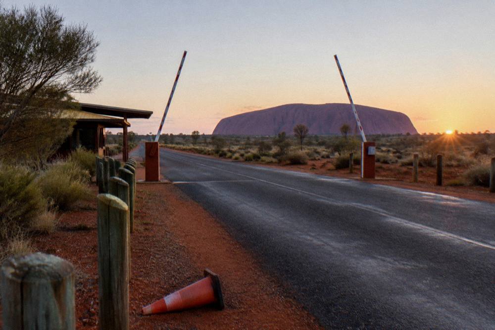 Open gate at the national park entry station at first light with a long empty road beyond