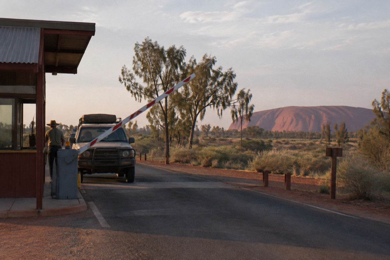 Entry station road sign at the boundary of Uluru-Kata Tjuta National Park under a wide desert sky