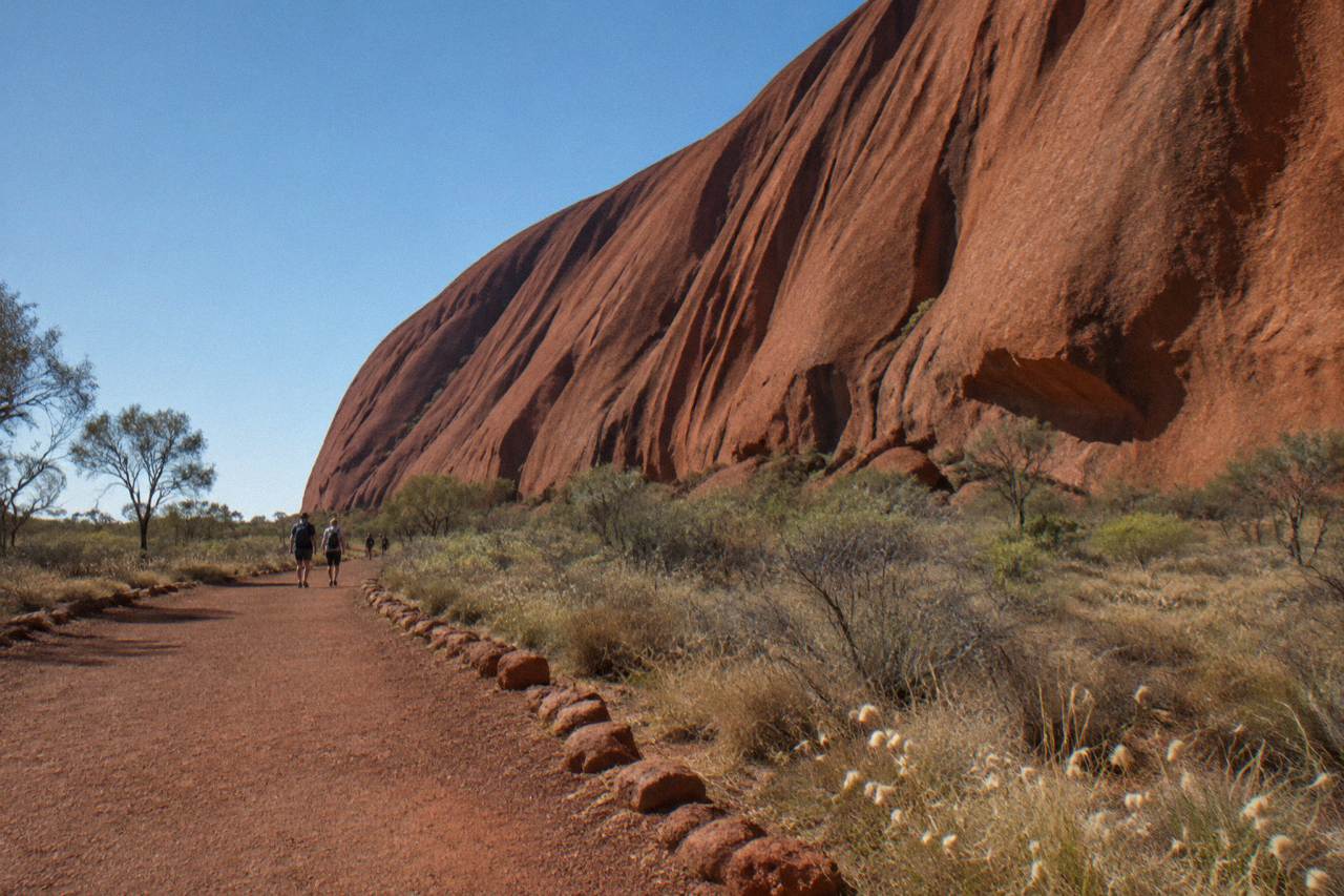 A paved desert path circling red rock walls under a wide blue sky at Uluru