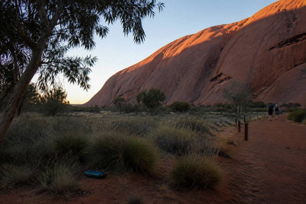 Walking path beside the base of Uluru at first light with smooth rock walls rising above the track