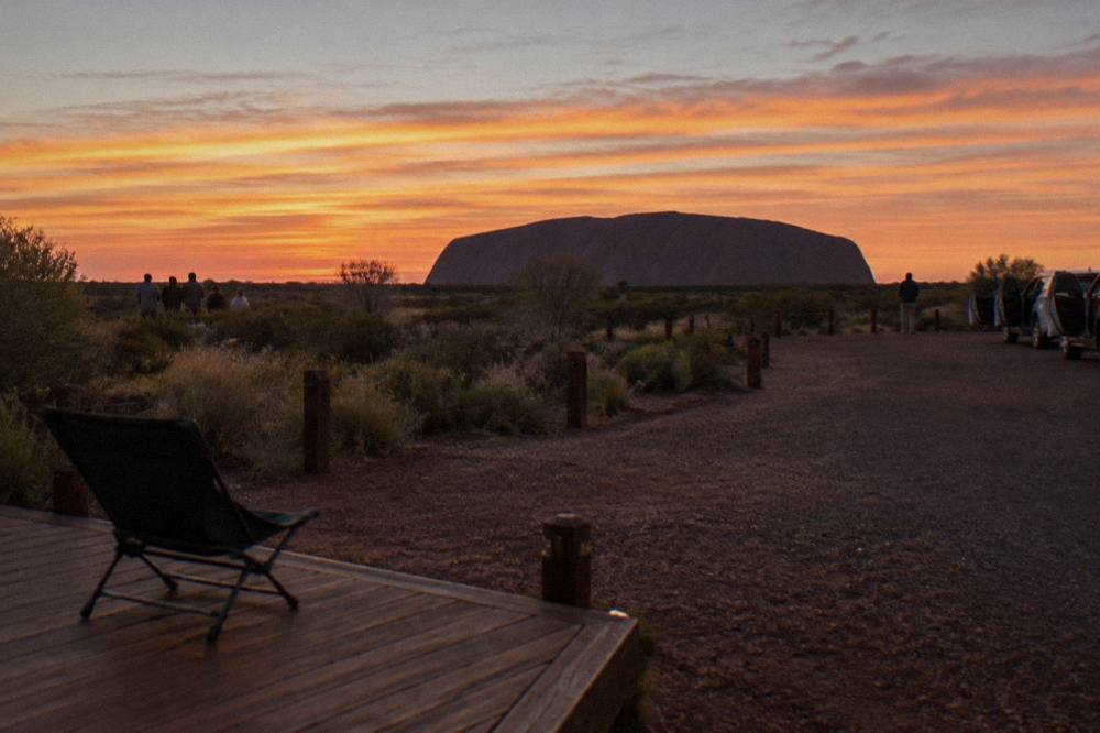 Uluru silhouetted against an orange evening sky with viewing area platform in the foreground