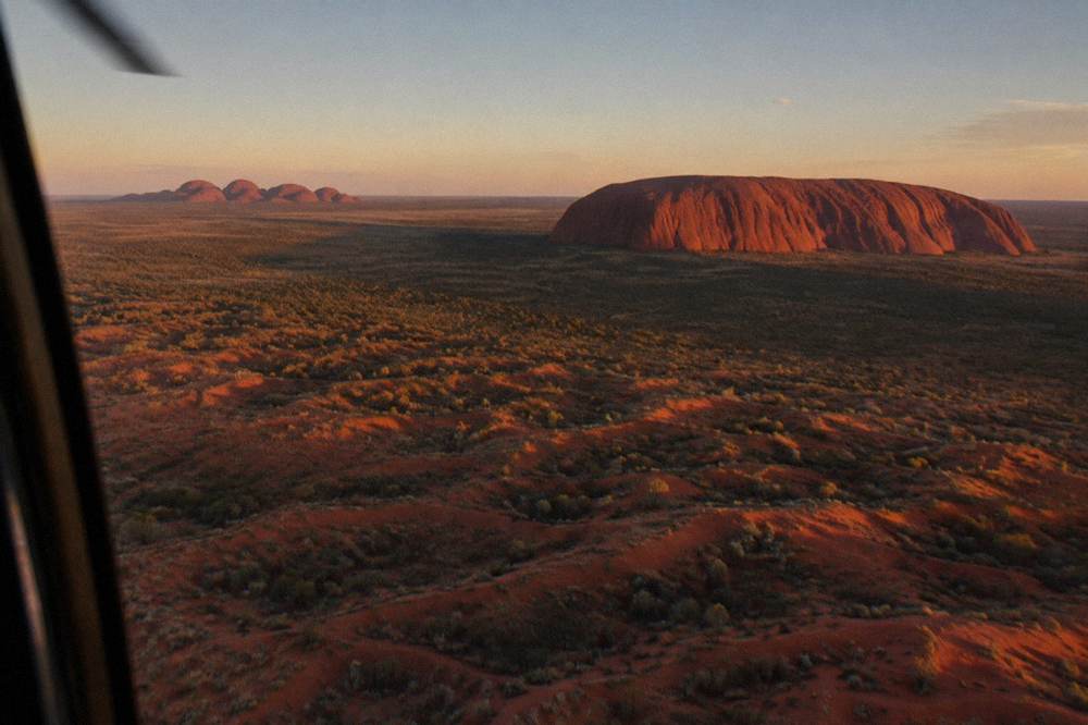 Aerial view of Uluru and surrounding desert dunes in low golden evening light from a helicopter