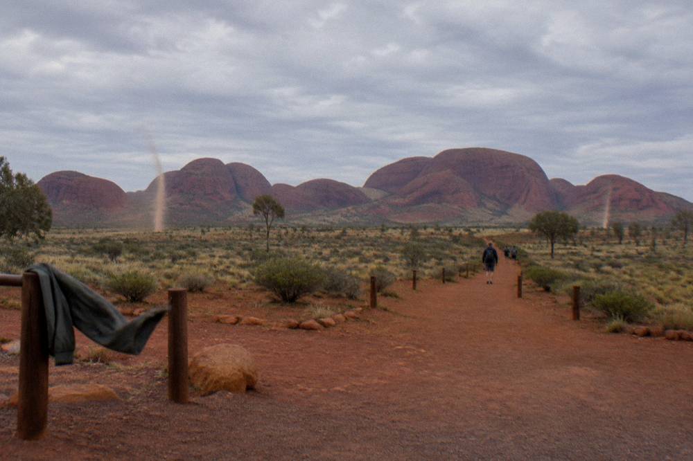 A marked walking track crossing open red earth toward distant rock domes under morning light