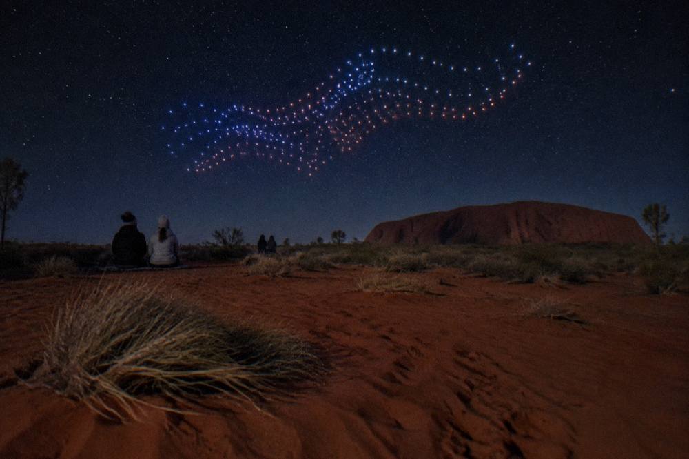 Hundreds of drone lights forming patterns in a dark sky over open desert