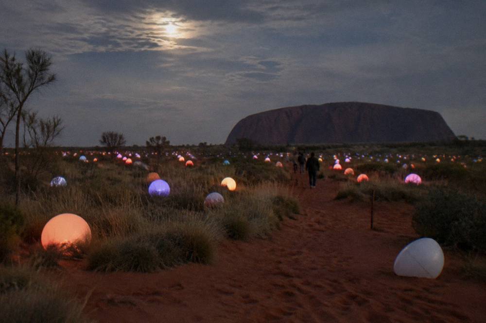 Rows of softly glowing coloured spheres scattered across red desert sand at night