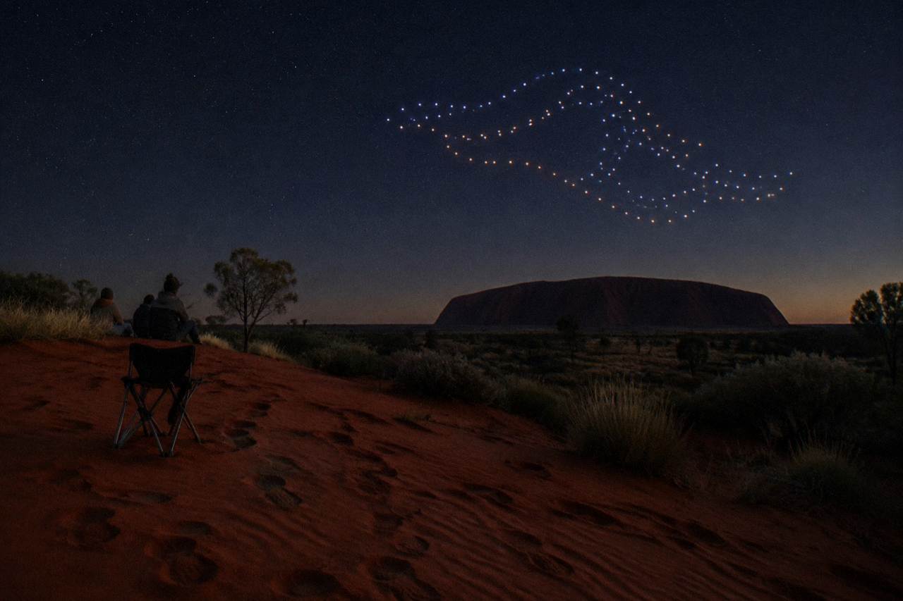Drone lights glowing in patterns above a dark desert plain near Uluru